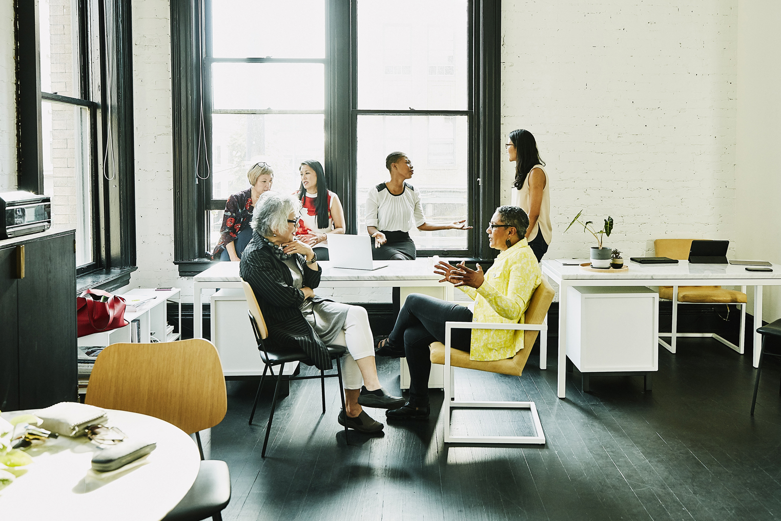 Six female coworkers in discussion during team meeting in creative office.