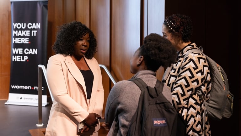 Three women conversing in a lobby, reflecting a moment of connection and engagement in a public space.