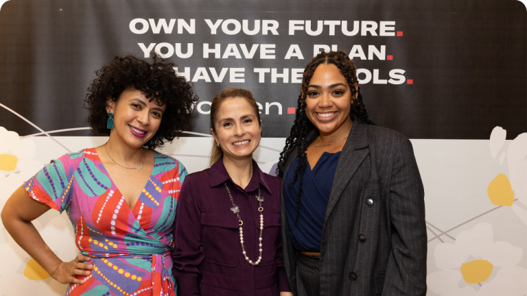 Women.NYC team members Sofia Mussa, Diana Franco, and Alexandra Martinez, stand together smiling in front of a sign that reads, Own your future. You have a plan. You have the tools. They appear confident and well-dressed, suggesting a professional or empowering event.