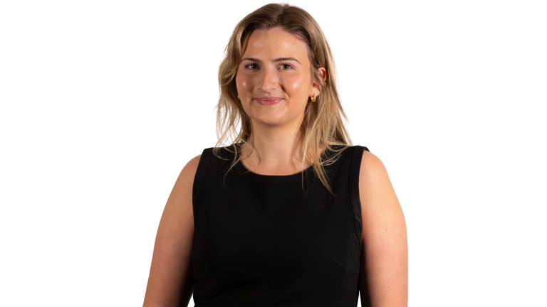 Julia Steinberg with long, light brown hair, wearing a sleeveless black dress, stands facing the camera and smiles against a white background.