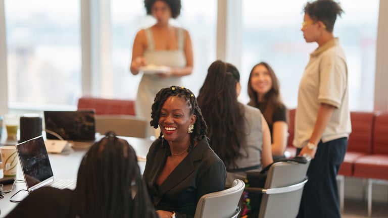 A woman smiling during a meeting with colleagues in a bright office.