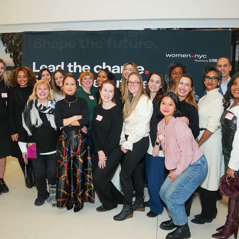 A large group of women posing for a photo in front of a banner that reads Shape the future. Lead the change.