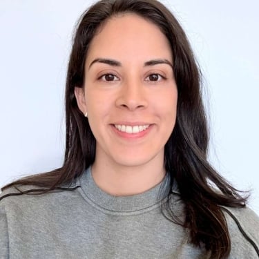 Fabianna Mercado with long dark hair, wearing a grey sweatshirt, smiles at the camera in front of a plain light-colored background.