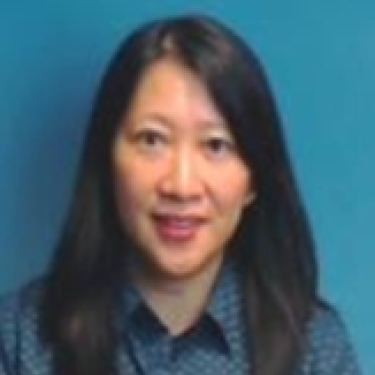 Woman with long black hair, Louise Li, wearing a blue-patterned shirt, sits in front of a solid teal background.