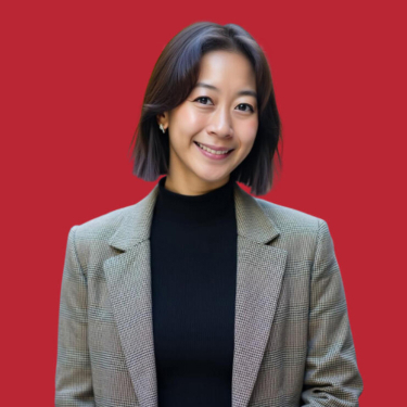 A smiling woman wearing a black turtleneck and a grey blazer against a red background.